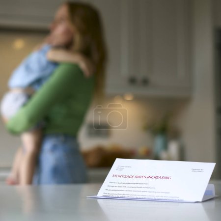 Madre acurrucándose hijo en casa con carta sobre el aumento de la tasa hipotecaria en el mostrador en primer plano