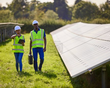 Male And Female Engineers Inspecting Solar Panels In Field Generating Renewable Energy