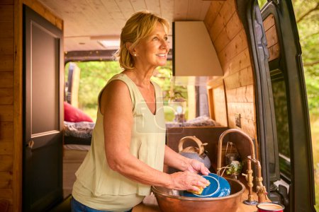 Senior Woman Enjoying Camping In Countryside Relaxing Inside RV And Doing Chores