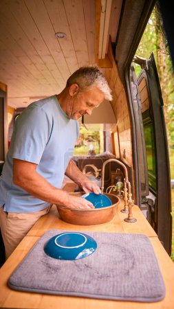 Senior Man Enjoying Camping In Countryside Relaxing Inside RV And Doing Chores