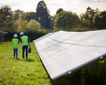 Rear View Of Male And Female Engineers Inspecting Solar Panels In Field Generating Renewable Energy