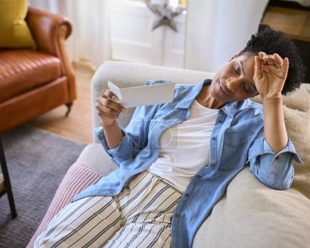 Menopausal Mature Woman Sitting On Sofa At Home Having Hot Flush Fanning Herself