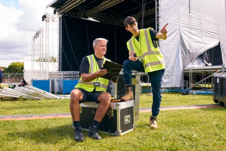 Männliches Produktionsteam mit Fluchtkoffern baut Freilichtbühne für Musikfestival auf