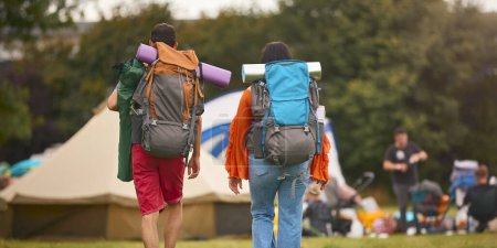 Rear View Of Young Couple Meeting At Summer Music Festival With Camping Equipment