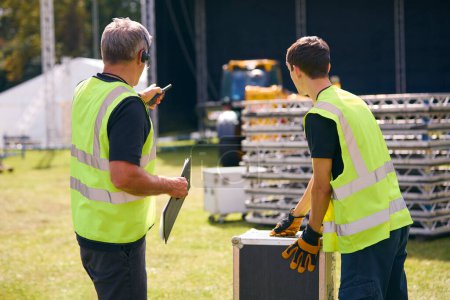 Equipo de producción masculino con auriculares que configuran el escenario al aire libre para el festival de música o el concierto