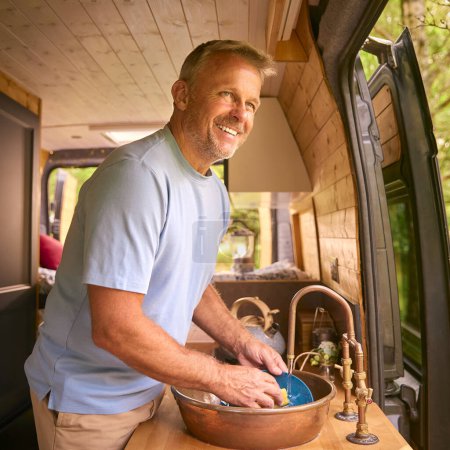 Senior Man Enjoying Camping In Countryside Relaxing Inside RV And Doing Chores