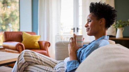 Mature Woman At Home Drinking Coffee Relaxing On Sofa In Lounge