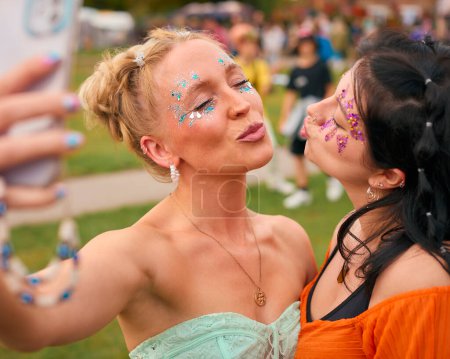 Two Female Friends Wearing Glitter Posing For Selfie At Summer Music Festival