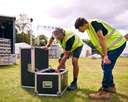 Männliches Produktionsteam packt Flugkoffer aus und baut Outdoor-Bühne für Musikfestival auf