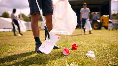 Primer plano de voluntarios recogiendo basura después de un evento al aire libre como concierto o festival de música