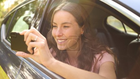 Frau im Auto auf Autoreise im Urlaub mit Handy fotografiert