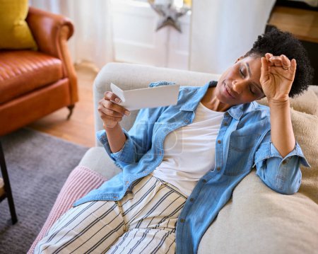 Menopausal Mature Woman Sitting On Sofa At Home Having Hot Flush Fanning Herself