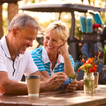 Seniorpaar sitzt nach Golfrunde beim Kaffee und schaut sich gemeinsam die Punktekarte an