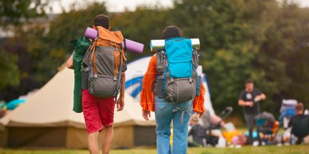 Rear View Of Young Couple Meeting At Summer Music Festival With Camping Equipment