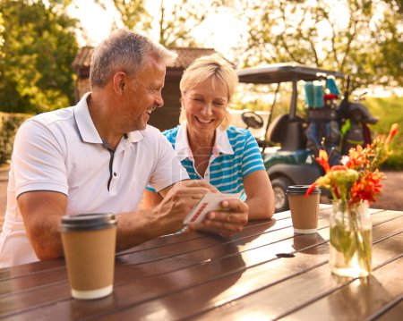 Seniorpaar sitzt nach Golfrunde beim Kaffee und schaut sich gemeinsam die Punktekarte an