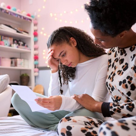Mother Comforting Teenage Daughter In Bedroom Looking At Letter With Disappointing Exam Results