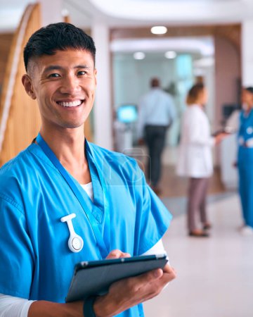 Porträt eines lächelnden männlichen Arztes oder einer Krankenschwester, die mit Kollegen im Hintergrund Peelings im Krankenhaus trägt