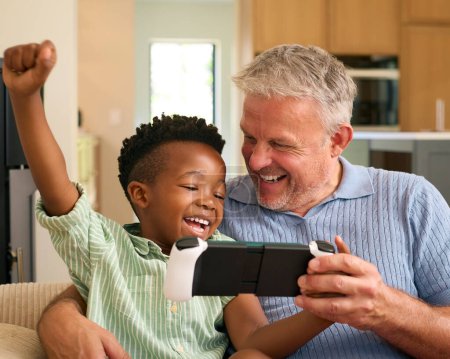 Familia multirracial con el abuelo y el nieto jugando en el dispositivo de juego portátil juntos