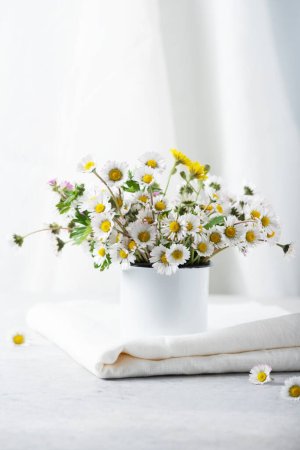 Téléchargez les photos : Concept de décoration confortable à la maison avec des fleurs de marguerite sauvage et nappe en lin blanc, image focus sélectif - en image libre de droit