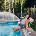 Funny portrait of smiling woman playing with dog and training golden retriever puppy in blue swimming pool. Popular dog breeds, outdoor activity and fun games with family pet on summer beach holiday.