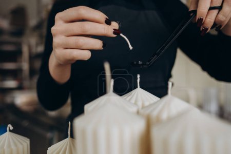 Woman cutting wick of homemade candle at table indoors, closeup