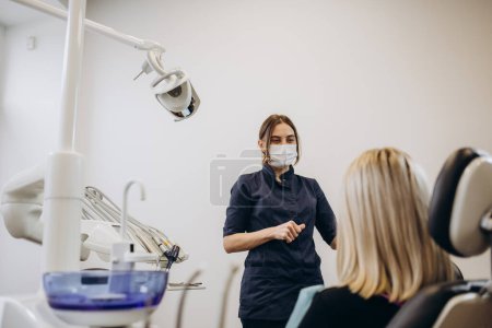 Foto de Dentista y paciente eligiendo el tratamiento en una consulta con equipo médico en el fondo - Imagen libre de derechos