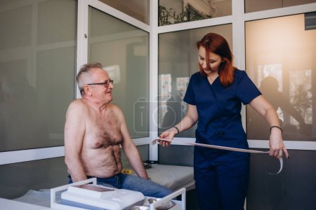 Téléchargez les photos : ECG montrant un bloc de branche bundle. Cardiologue examinant un patient âgé avec un appareil Holter dans le département de cardiologie de l'hôpital. Homme mûr sur le canapé de la clinique - en image libre de droit
