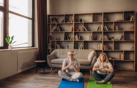 Foto de La pareja de ancianos está haciendo entrenamiento físico en casa. Haciendo yoga juntos. concepto de estilo de vida saludable - Imagen libre de derechos