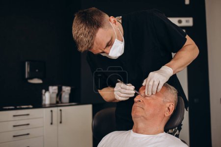 Photo for A plastic surgeon examines an older gray-haired man. - Royalty Free Image