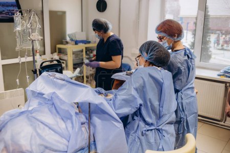 Foto de El equipo de cirujanos uniformados realiza una operación de corrección de venas varicosas en un paciente en la clínica de cirugía
. - Imagen libre de derechos