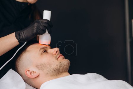 Photo for Young woman getting chromotherapy procedure for face skin rejuvenation. - Royalty Free Image