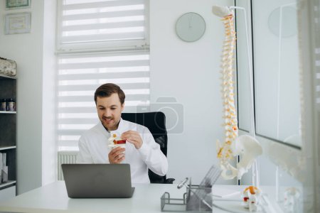 Photo for A vertebrologist doctor works on a camera behind a laptop. - Royalty Free Image