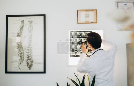 Photo for A vertebrologist doctor looks at an X-ray with a patient in a hospital office. - Royalty Free Image