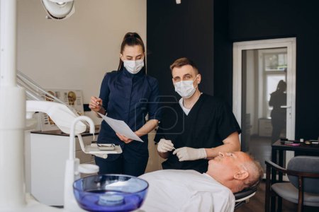 Photo for Handsome old man talking to the dentist. Female doctor and senior man in the dentist's office. Grandfather looking into the mirror on his teeth. Stock photo - Royalty Free Image