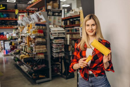 Photo for Young independent woman buying paint roller and tools for house decoration in hardware store. - Royalty Free Image