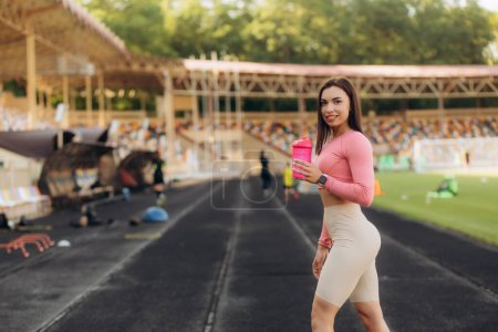 Téléchargez les photos : Portrait de femme heureuse tenant une bouteille d'eau sur les pistes de course - en image libre de droit
