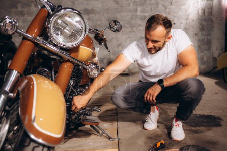 Photo for A man is repairing his retro motorcycle in the garage. - Royalty Free Image