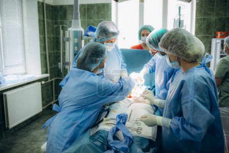 Photo for Surgeons perfoming surgery operation of abdominal cesarean section during child delivery birth at clinic operating room. - Royalty Free Image