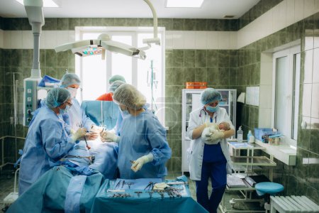 Photo for Surgeons perfoming surgery operation of abdominal cesarean section during child delivery birth at clinic operating room - Royalty Free Image