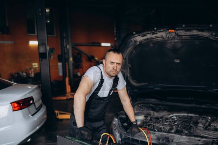 Photo for Hands of auto mechanic include the installation of refilling the air conditioner in car service. - Royalty Free Image