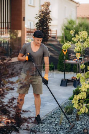 Photo for The gardener uses a rake to level decorative stones. - Royalty Free Image
