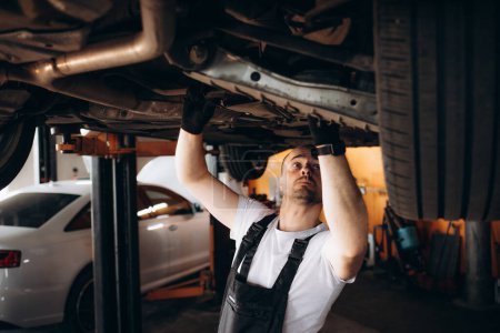 Photo for Car caucasian man wearing work clothes for safety in working in large garages, prevents fouling, mechanic car wheel, with raised car repair undercarriage car, check lower parts that need be repaired. High quality photo - Royalty Free Image
