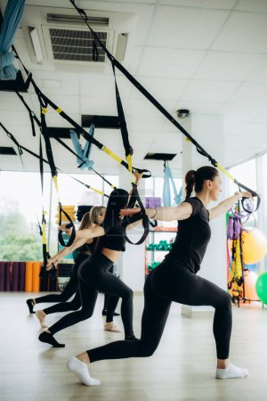 Photo for Group of active sports girls in black sportswear are engaged in budgie fitness in the gym. Bungee jumping in the gym. High quality photo - Royalty Free Image