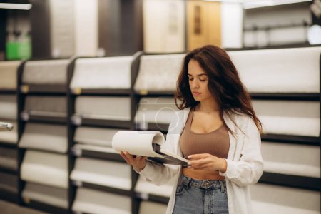 Photo for A woman is looking at a wallpaper catalog in a hardware store. - Royalty Free Image