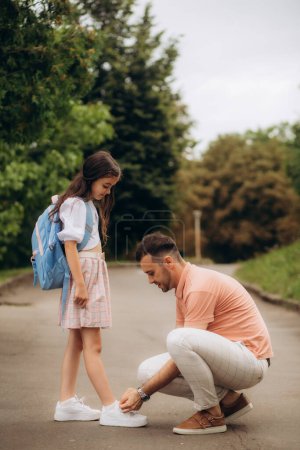 Foto de La niña va a la escuela. Papá ata los zapatos de su hija.. - Imagen libre de derechos