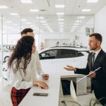 Sales manager showing car charging station to a young couple, selling electric cars in the showroom. Concept of buying eco-friendly car for family. High quality photo