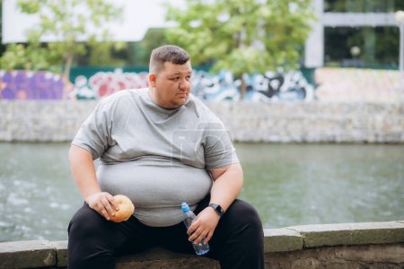 Fat man eating a burger and water in training at the stadium.