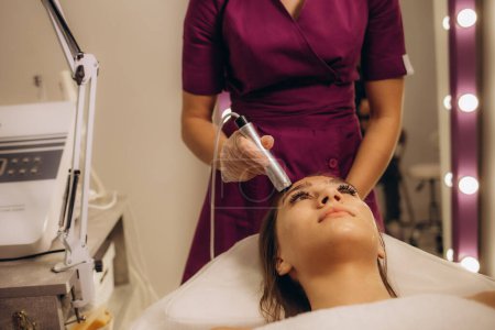 Foto de Primer plano de la mujer cabeza recibiendo fonofóresis electroporación terapia facial en salón de spa de belleza. Foto de alta calidad - Imagen libre de derechos