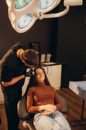 Photo for Doctor is examining beautiful young woman's face using a special equipment. High quality photo - Royalty Free Image