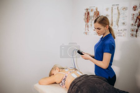 Téléchargez les photos : Une patiente âgée utilise une thérapie de stimulation électrique TENS sur son dos - en image libre de droit